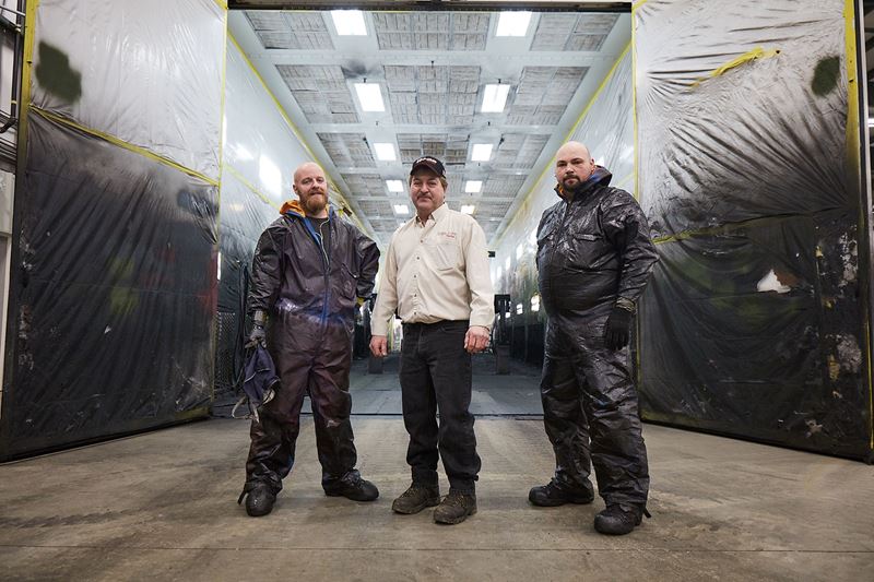 3 men in a row in front of a commercial paint shop